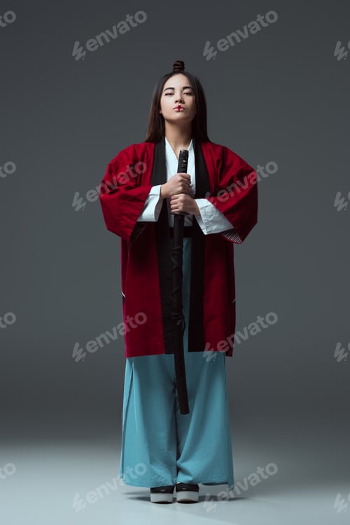 Preview: full length view of samurai in kimono holding katana sword and looking at camera on grey