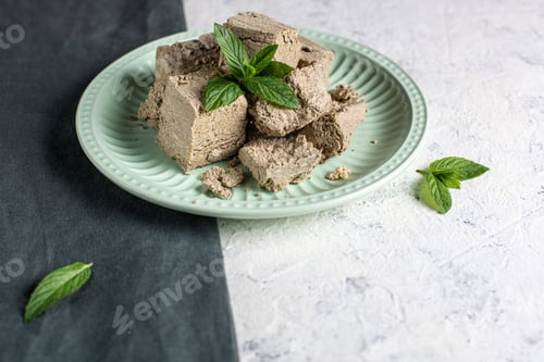 Preview: Pieces of halva on green plate. Sweet dessert with mint leaves on white background