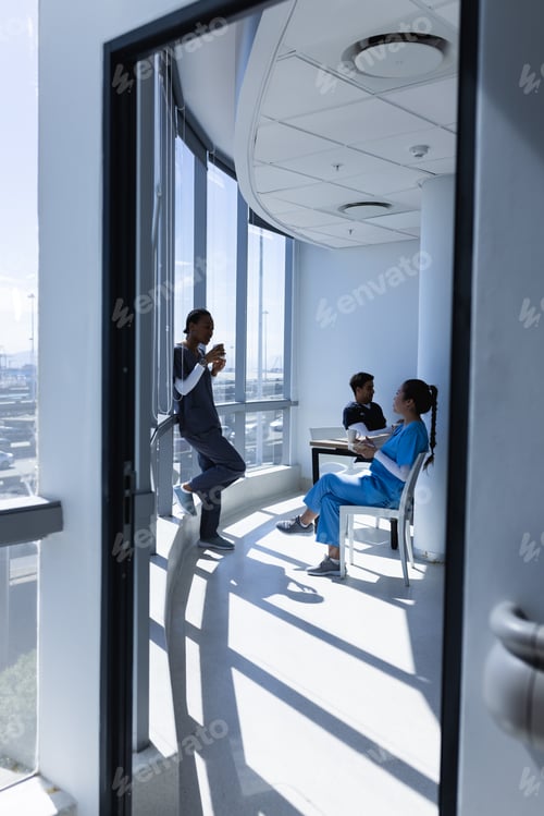 Preview: Diverse male and female doctors talking, drinking coffee and eating lunch in sunny hospital