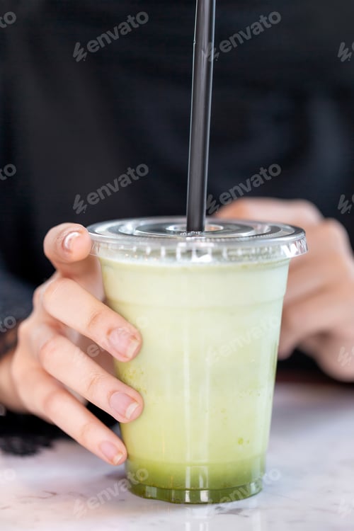 Preview: Female hand holding freshly made avocado juice, closeup