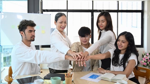Preview: Happy motivated business people stacking hands together, showing support and team spirit.