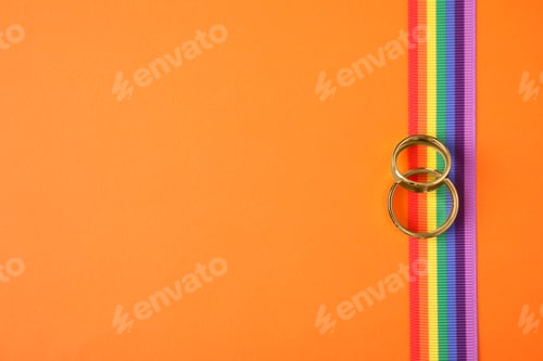 Preview: Top view of wedding rings and rainbow ribbon on color background, space for text. Gay symbol