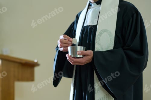 Preview: Priest of Catholic church in cassock holding small cup with unleavened bread