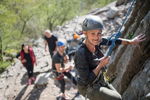 Preview: Group of seniors with instructor climbing rocks outdoors in nature, active lifestyle
