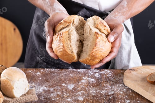Preview: Close-up midsection of african american male baker breaking baked bread over table
