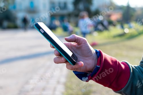 Preview: Hand consulting a smartphone, with the screen free to fill, in an outdoor park