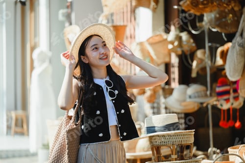 Preview: Young tourist adjusting her straw hat while visiting a traditional Thai market