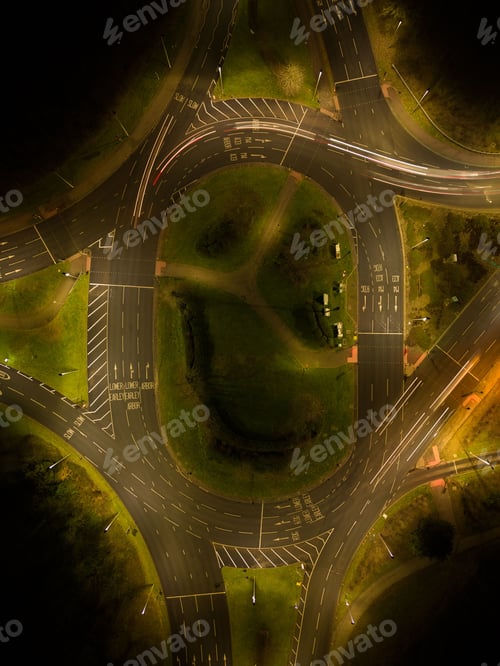 Preview: Top view of a bustling nighttime intersection surrounded by lush green trees and foliage