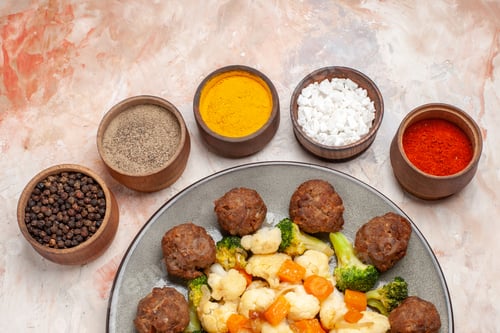 Preview: front view broccoli and cauliflower salad and meatball on plate different spices in small bowls on