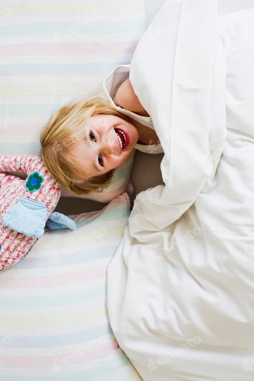 Preview: Portrait of young girl lying in bed with toy elephant