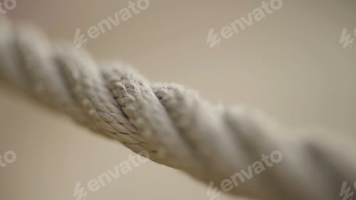 Preview: Extreme close up of a rope on blurred beige background. Action. Macro view of a stretched beige rope
