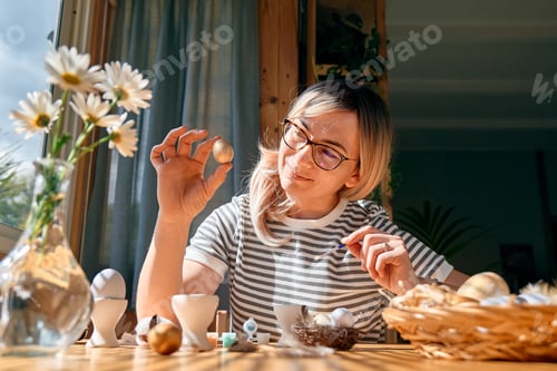 Preview: Smiling woman preparing easter decoration at home, painting colorful easter eggs.