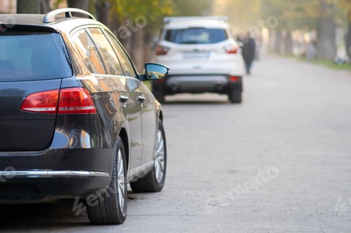 Preview: Cars parked in a row on a city street side on bright autumn day
