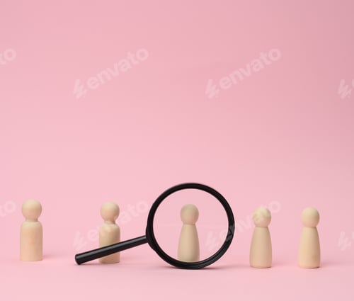 Preview: Wooden figures of men stand on a pink background and a black magnifying glass. Recruitment concept