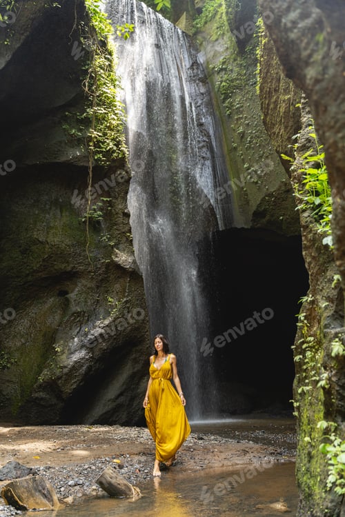 Preview: Pleased young tourist walking near picturesque waterfall