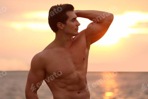 Preview: Handsome young man posing on beach near sea at sunset