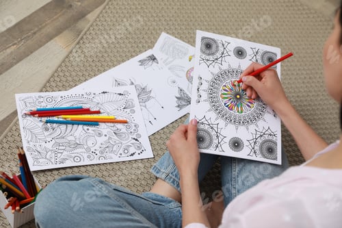 Preview: Young woman coloring antistress page on floor, closeup