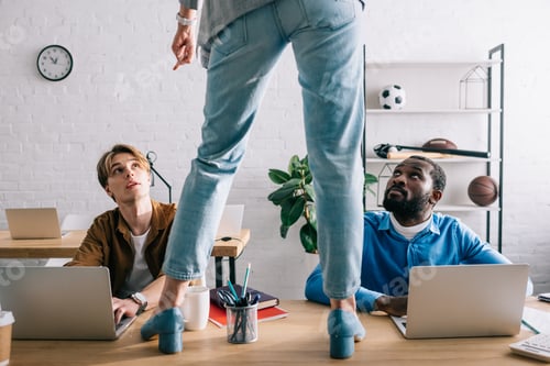 Preview: cropped image of female standing on table and pointing by finger to two multicultural businessmen
