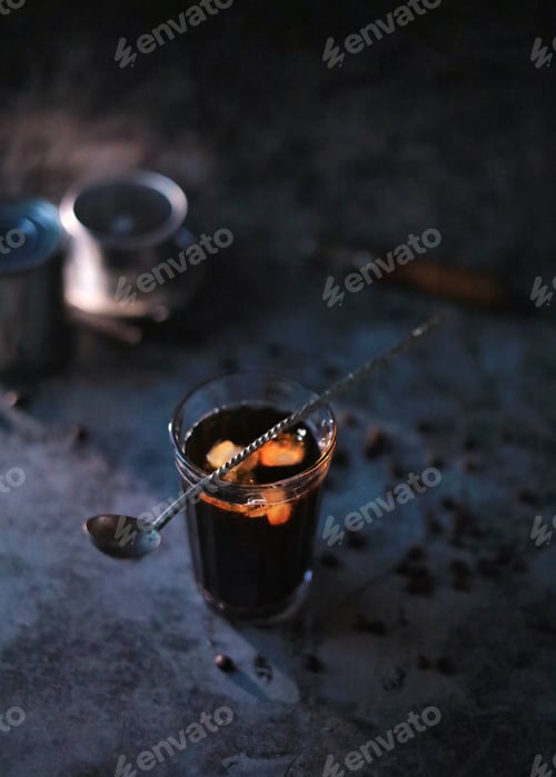 Preview: Iced coffee in a faceted glass with a spoon on top on a dark background