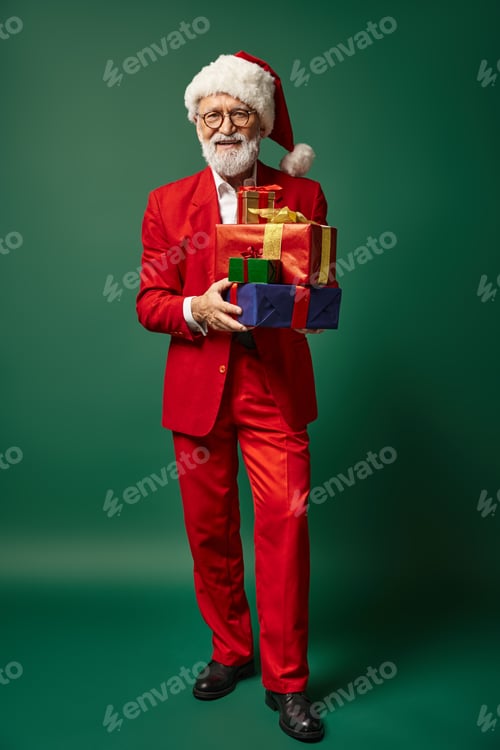 Preview: elegant Santa in red stylish attire holding pile of presents on green backdrop, winter concept