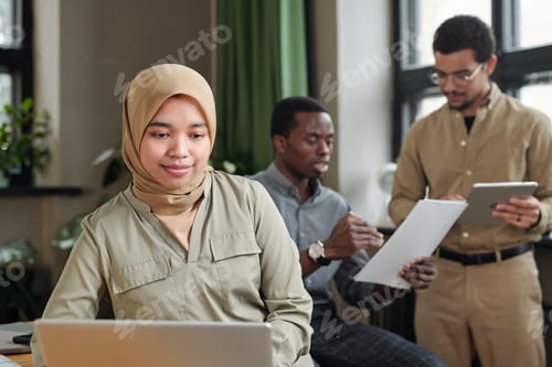 Preview: Young Muslim businesswoman in hijab sitting in front of laptop