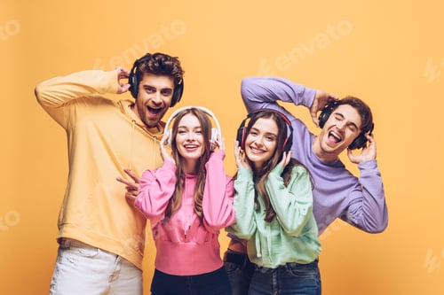 Preview: smiling friends listening music in headphones and dancing together, isolated on yellow