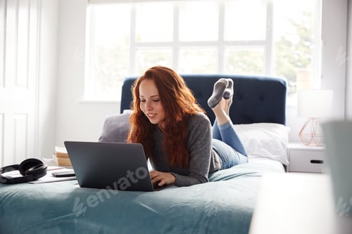Preview: Female College Student Lies On Bed In Shared House Working On Laptop