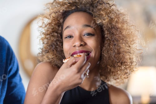 Preview: Young woman eating party food in kitchen