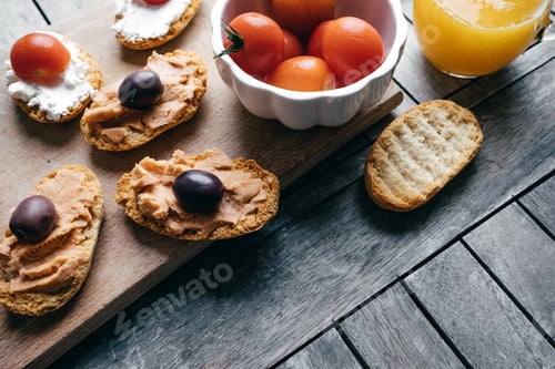 Preview: Bruschetta with soft cream cheese, olives, cherry tomatoes, pate and orange juice on wooden table