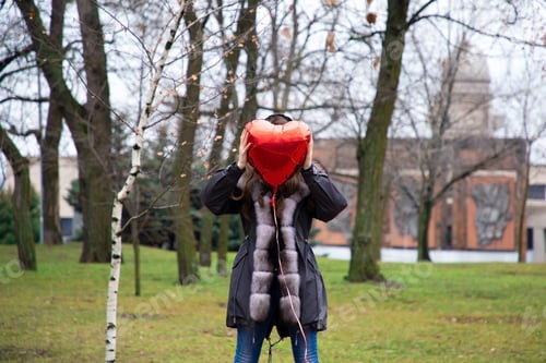 Preview: young woman walking in the park with a heart-shaped balloon