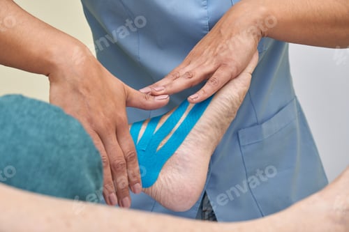 Preview: Female physiotherapist applying blue kinesio tape on woman's leg