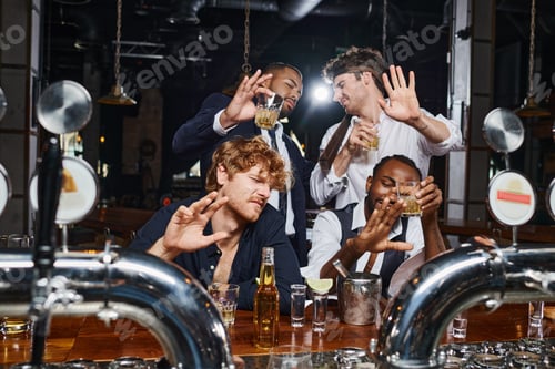 Preview: four drunk multicultural friends covering faces from bright light, tequila shots, beer and whiskey