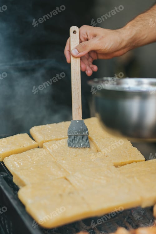 Preview: Hand of a man greasing polenta with a cooking brush on the grill