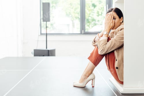 Preview: scared businesswoman in formal wear sitting on floor in conference hall