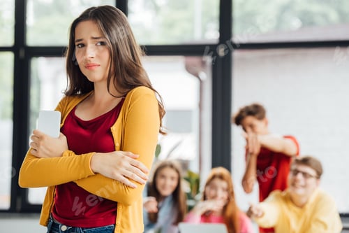 Preview: group of schoolchildren bullying sad girl with smartphone