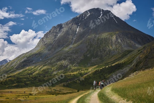 Preview: Hikers trek on a path in the mountains during daytime under a blue sky