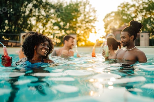 Preview: Group of friends enjoying drinks in swimming pool at sunset