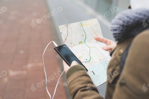 Preview: Over shoulder view of female backpacker with smartphone looking at map on city sidewalk