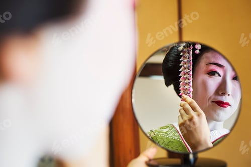 Preview: A woman made up in the traditional geisha style, with an elaborate hairstyle and floral hair clips,