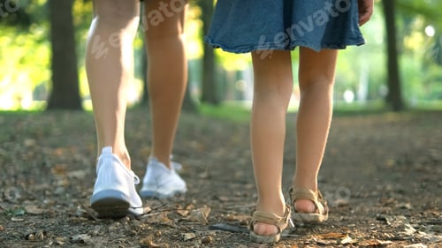 Preview: Mom and her small daughter with long hair walking together holding hands in summer park.