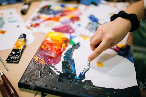 Preview: A kid's hand paints a picture with a palette knife and bright acrylic paints