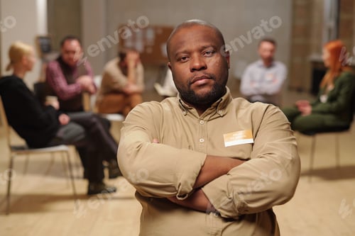 Preview: Serious African man crossing arms by chest against group of people