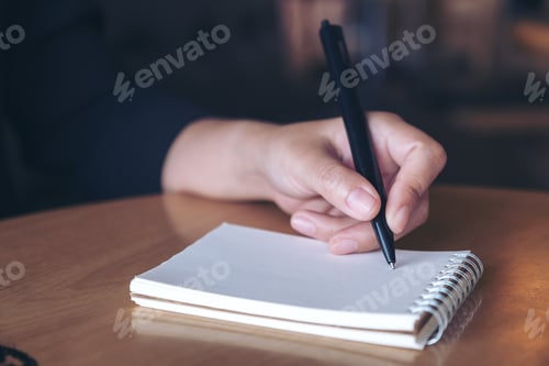 Preview: Closeup image of a hand writing down on a white blank notebook on table