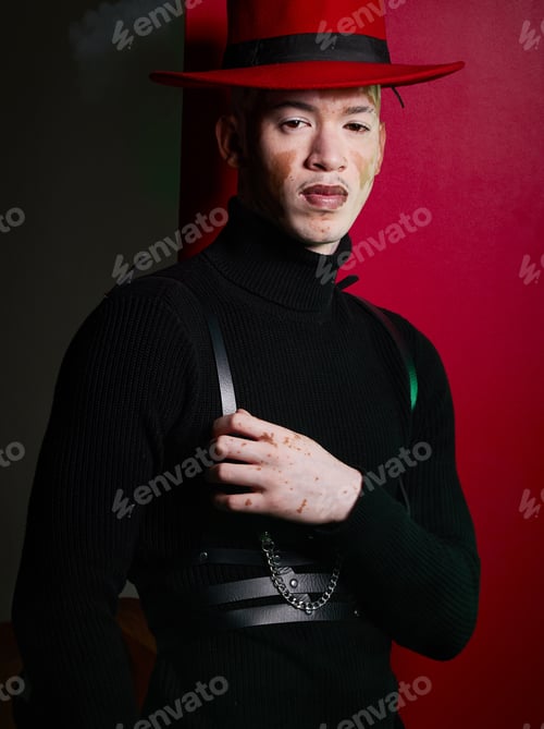 Preview: Portrait, fashion and stylish man with vitiligo posing on a red studio background looking confident
