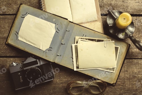 Preview: Old photographs and a camera on a wooden table with an empty notebook and a candle