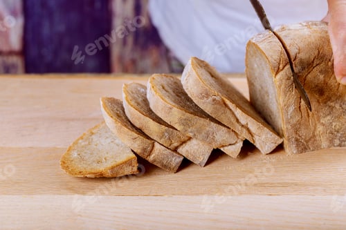 Preview: Fresh whole grain bread on kitchen table or wooden bread board with man holding bread knife and