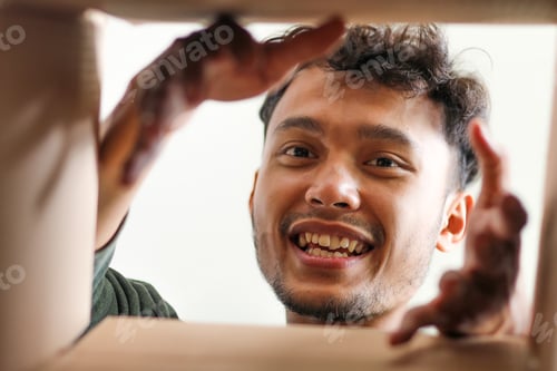 Preview: Excited Young Asian Man Smiling And Reaching Into Box