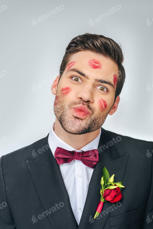 Preview: portrait of handsome groom in suit with red lipstick on face isolated on grey