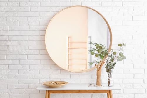 Preview: Big round mirror, table with jewelry and decor near brick wall in hallway interior