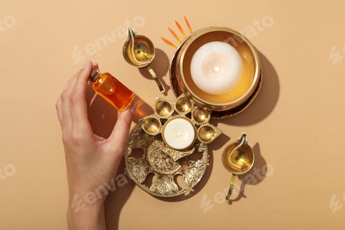 Preview: Copper oriental utensils, bottle of oil in hand and candles on beige background, top view